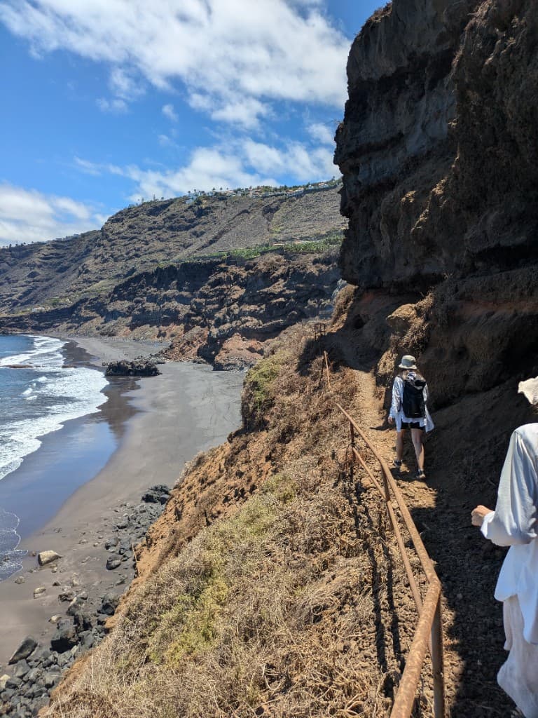 Hikers on a cliff path above a black sand beach